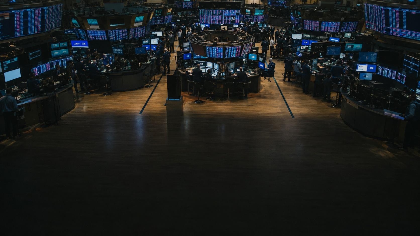 Vista elevada del piso de operaciones de la Bolsa de Nueva York. Puestos en herradura con pantallas encendidas, paneles de datos cubriendo las paredes, y grupos de operadores de traje trabajando entre ellos. El piso de madera del primer plano está vacío y en penumbra.